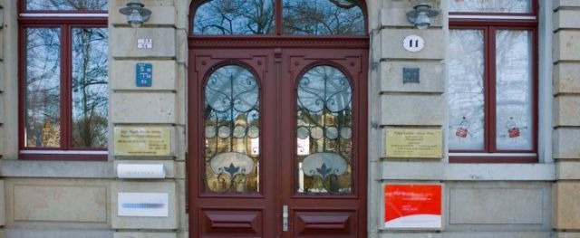 Eingang eines historischen Gebäudes mit großen Doppeltüren und Fenstern.