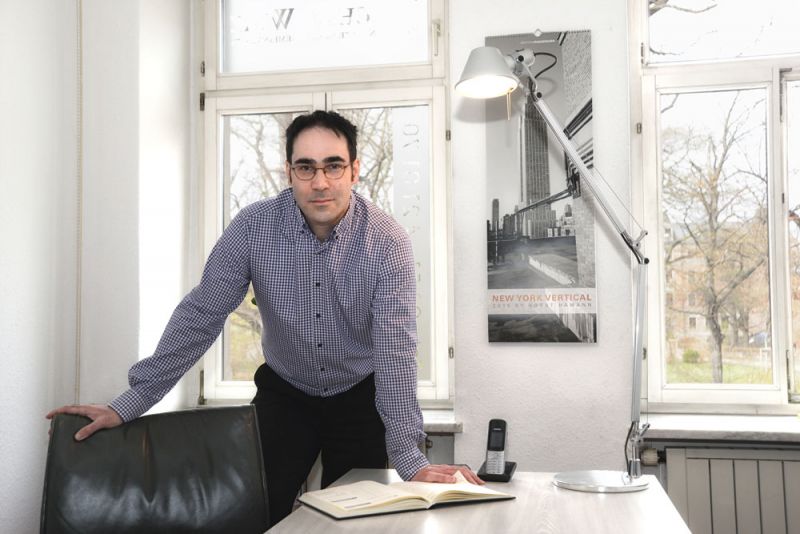 Mann steht an einem Tisch in einem hellen Raum mit Fenster und modernen Möbeln.